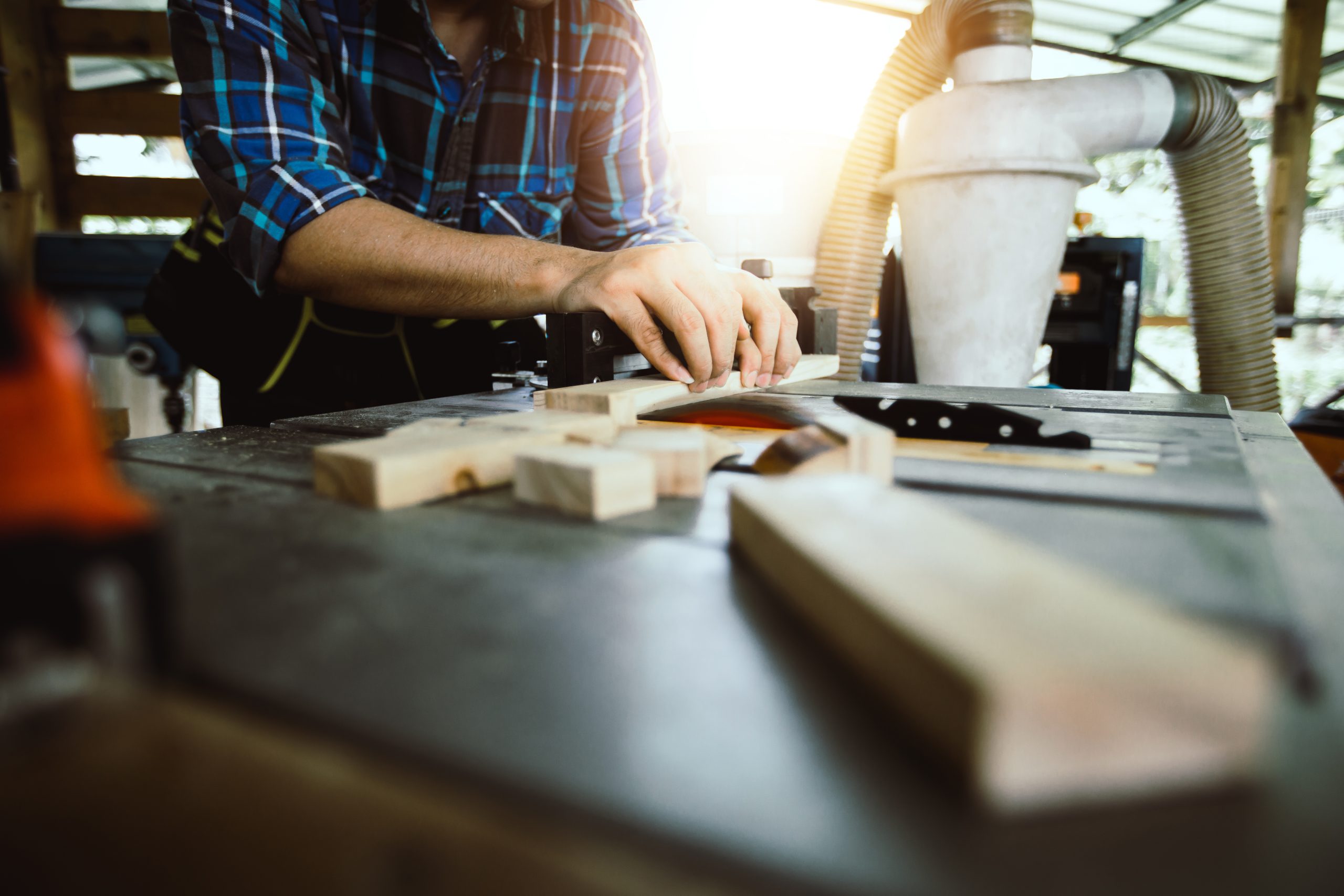 Carpenter cutting timber on a table saw in a bright workshop with offcuts on the bench