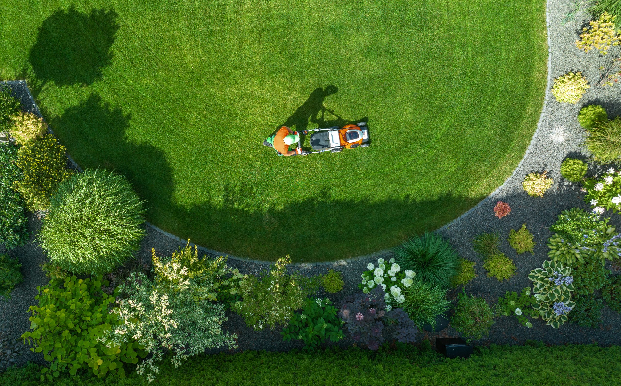 Landscaping in Essex: aerial view of a lawn being mowed beside neat planted borders and a gravel path by Latten Building Projects